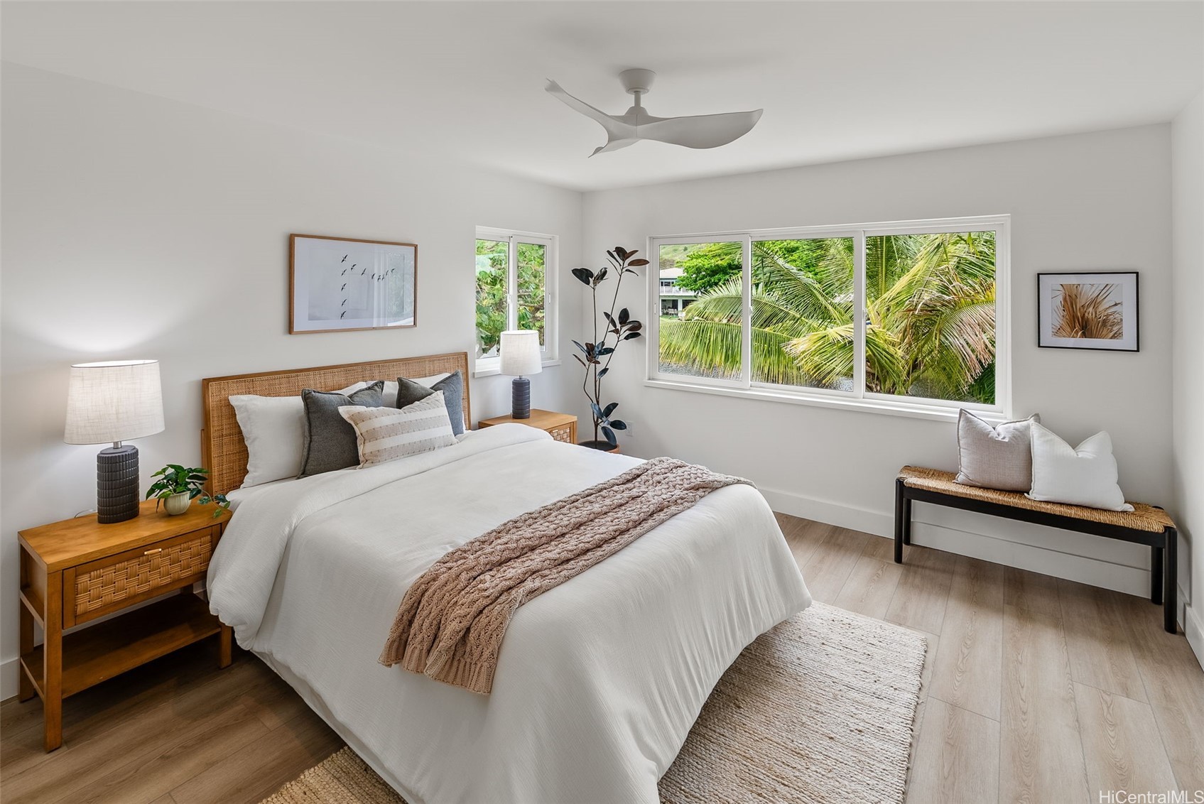 Staged bedroom with a white bed and wide windows overlooking palm foliage.