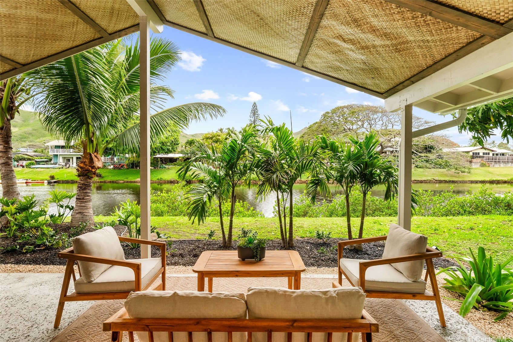 Covered lanai with wooden seating and tropical palms overlooking a canal.