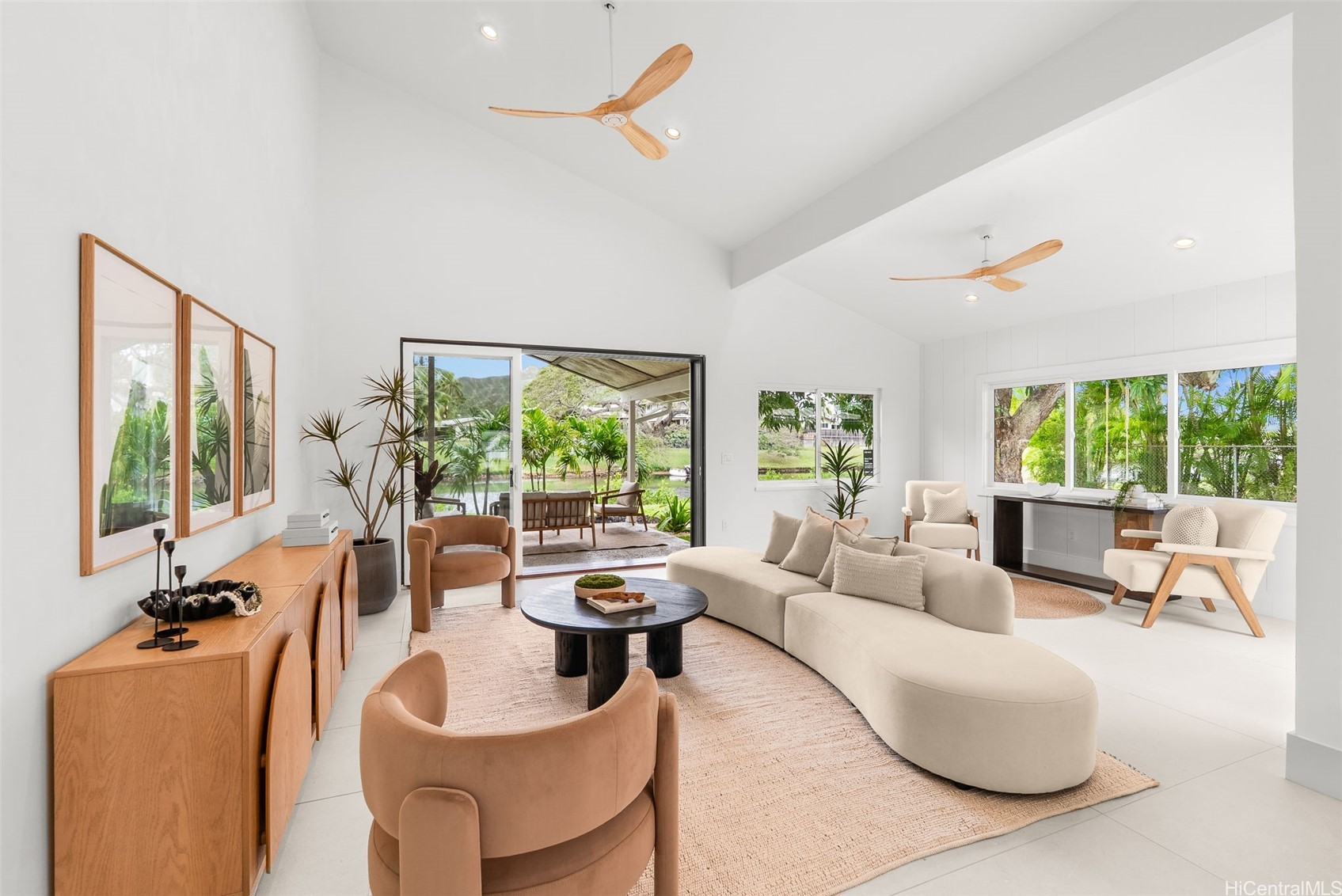 Staged living room with a vaulted ceiling, cream sectional, and sliding doors opening to a tropical lanai.