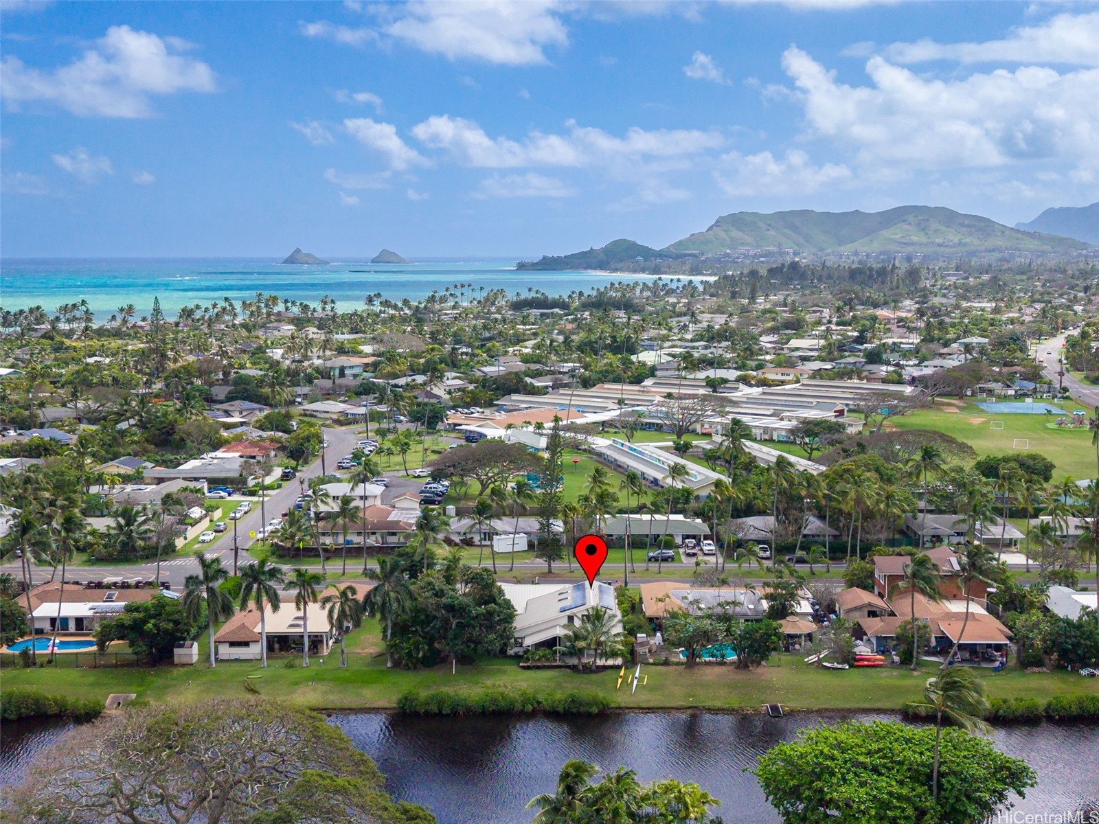 Aerial view of 1251 Kainui Drive near Kailua’s coastline, with homes, canal, ocean, and mountains.