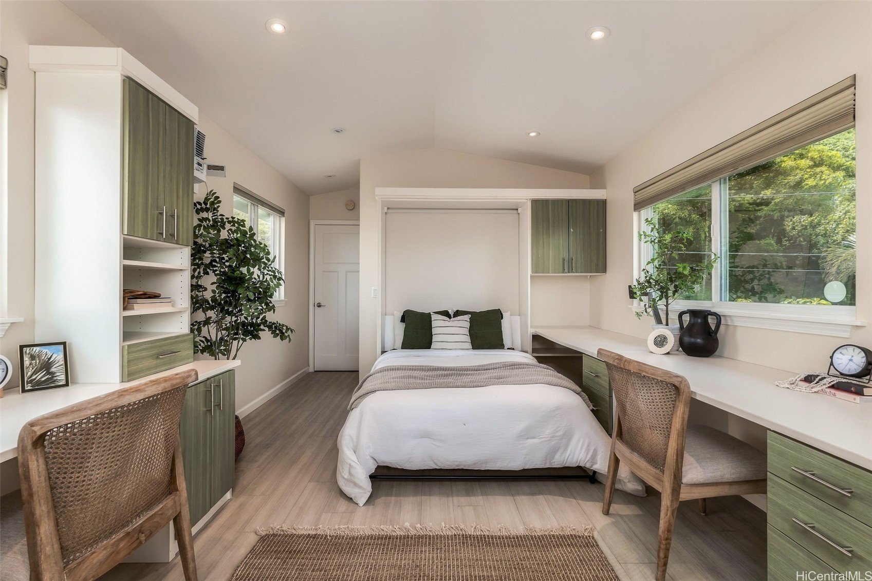 Bedroom with a built-in Murphy bed, green cabinetry, and desks beside a large window.