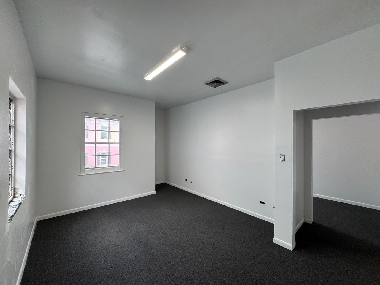 Empty office with dark carpet, two windows, and a doorway to an adjoining room.