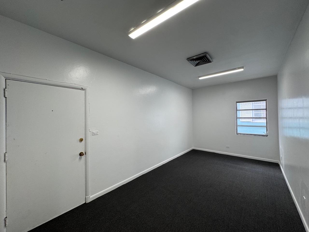 Empty office with dark carpet, white walls, and a window.