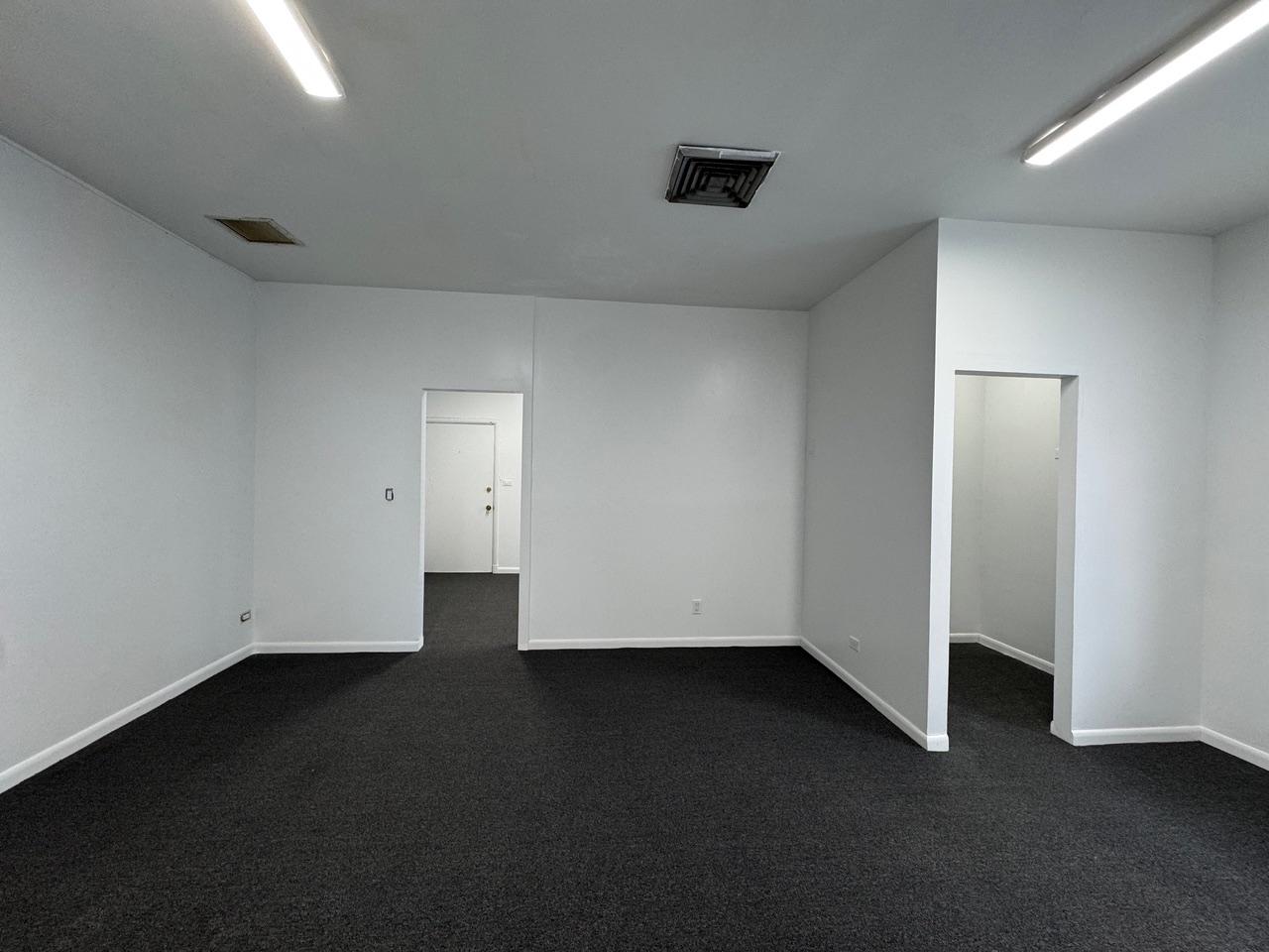 Vacant office with dark carpet, fluorescent lights, and two open doorways.