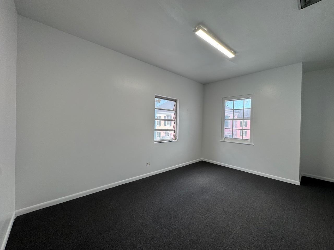 Empty office with dark carpet, white walls, and two windows.