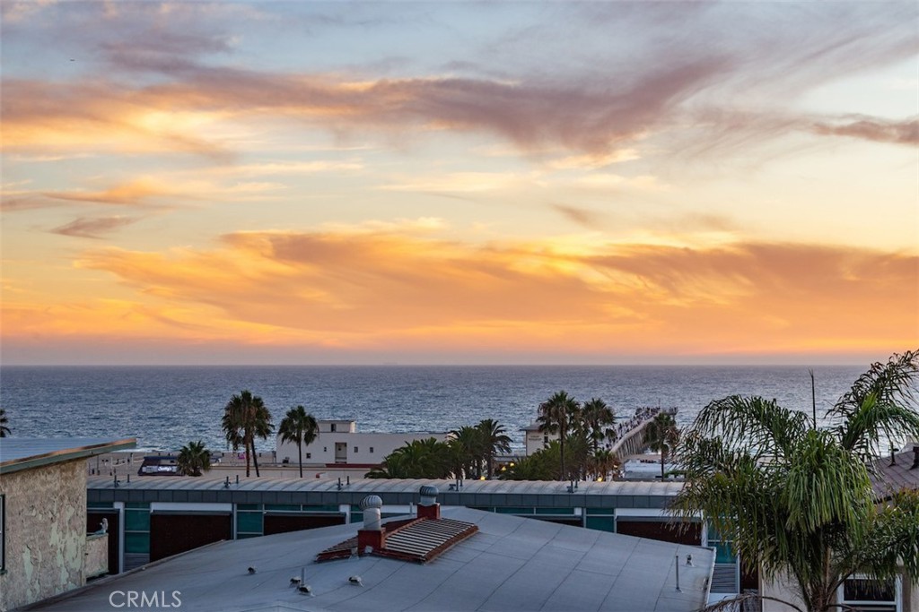 Ocean view at sunset beyond palm-lined rooftops.