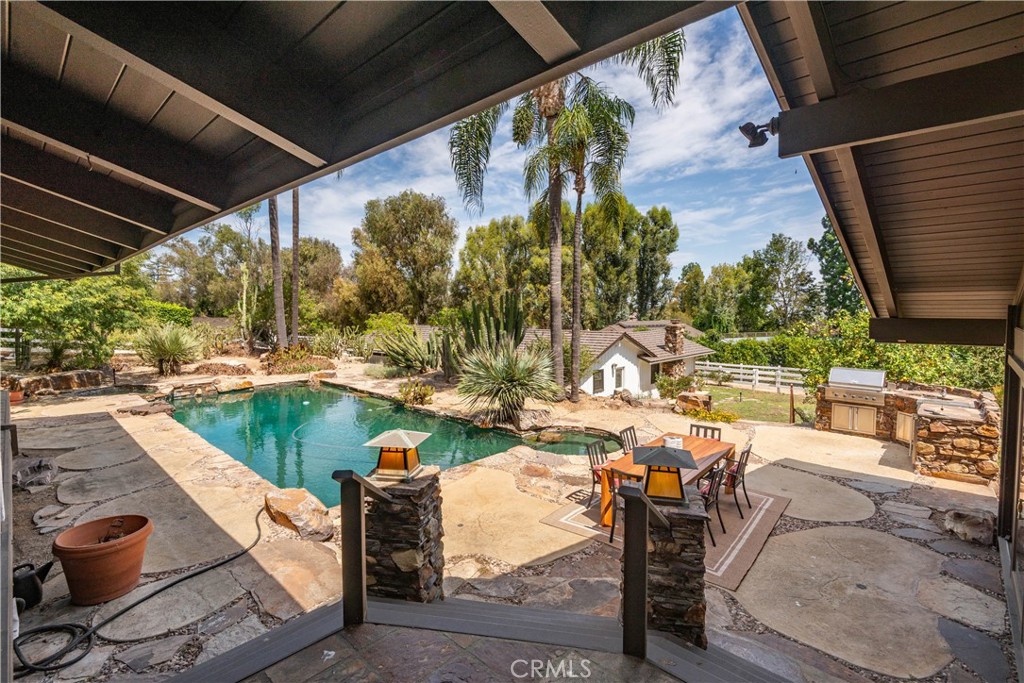 Backyard pool and stone patio with outdoor dining area and barbecue.