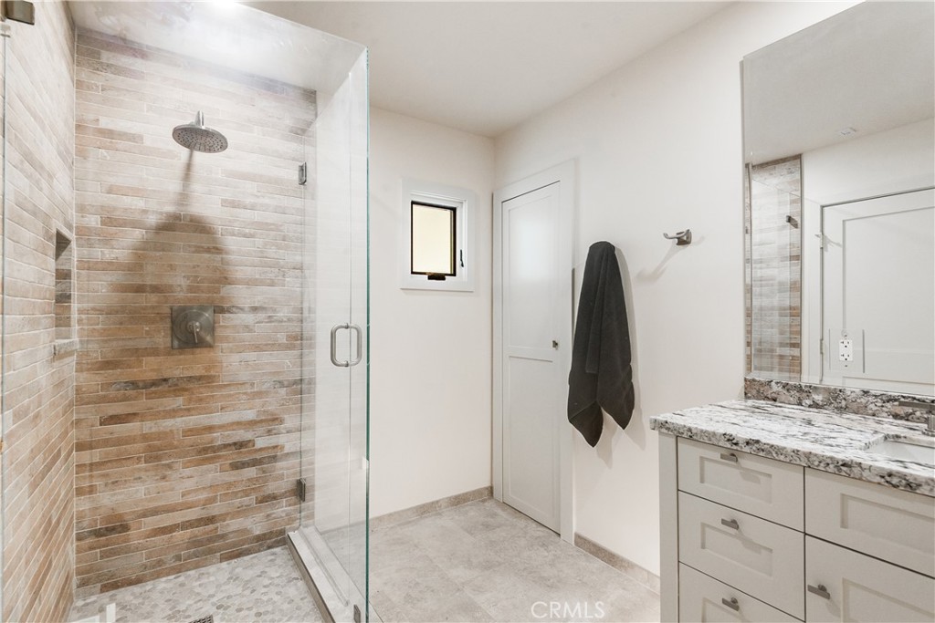 Bathroom with a glass-enclosed stone-look tile shower and white vanity with a marble-pattern countertop.