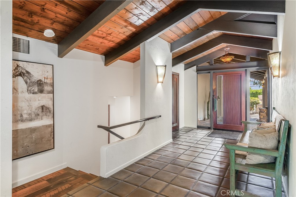 Entry foyer with an exposed wood-beam ceiling, tiled floor, and glass-paneled front door.