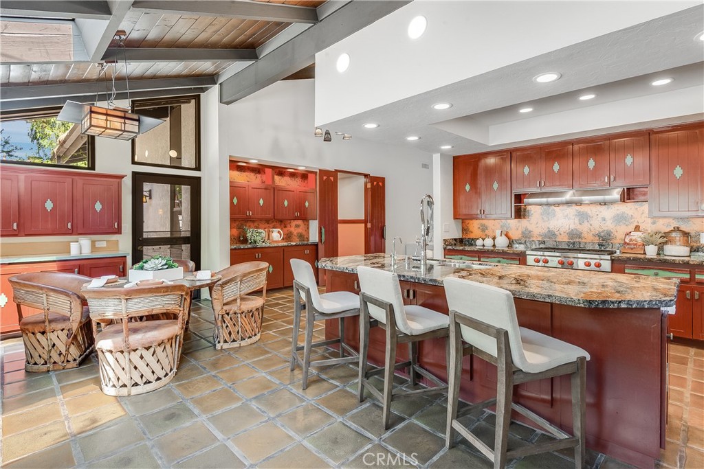 Kitchen with a large granite island, reddish wood cabinets, and a woven dining set.