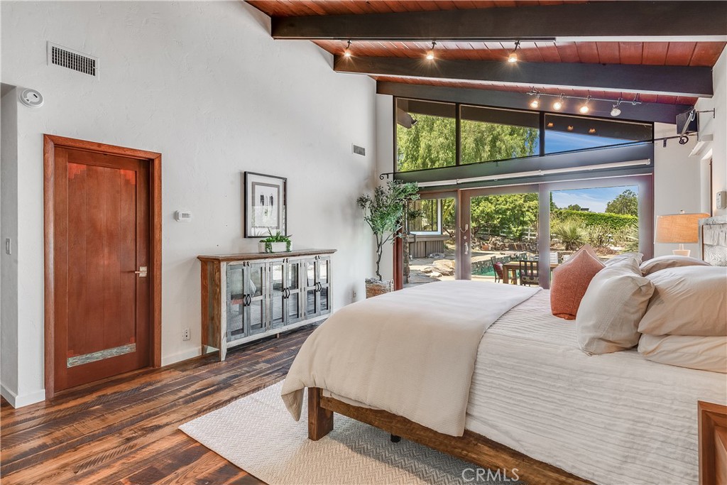 Bedroom with exposed wood ceiling beams and tall windows overlooking a garden.