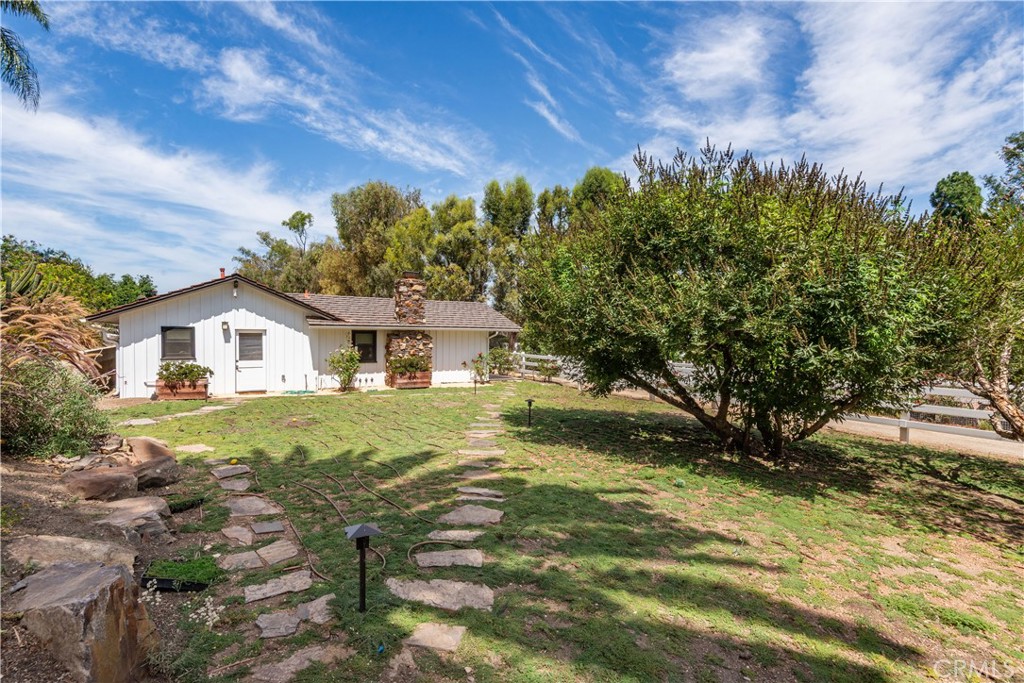 Single-story white house with a stone chimney, grassy yard, stepping-stone path, and mature trees.
