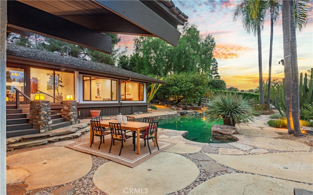 Backyard pool and stone patio with outdoor dining area beside the home at sunset.