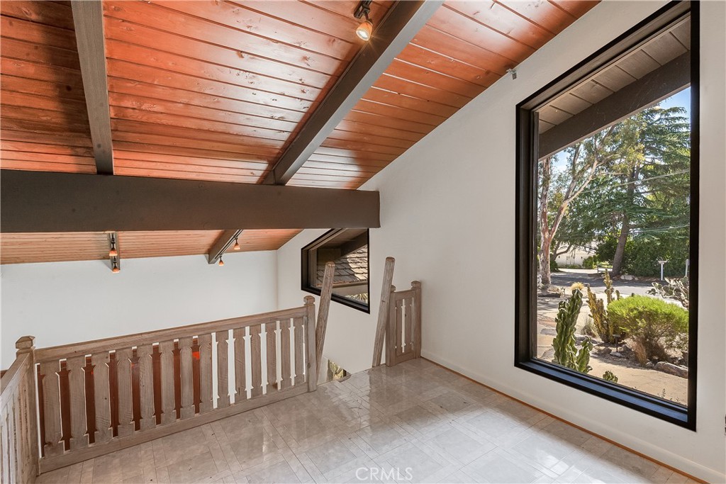 Upstairs landing with a wood-plank ceiling, pale railing, and large window overlooking a landscaped yard.