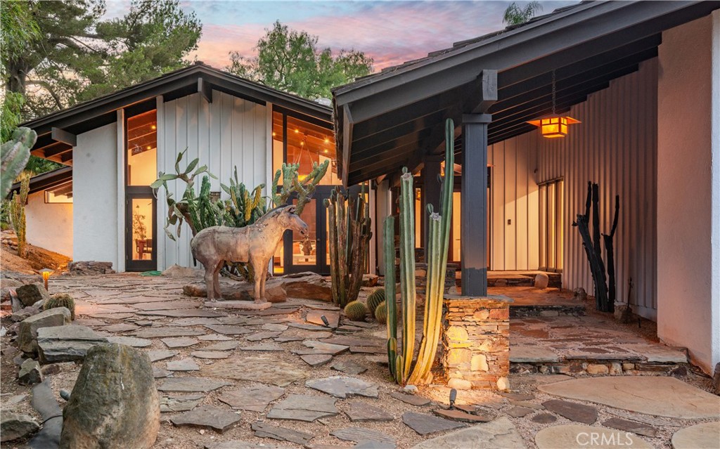 Modern home at dusk with a stone courtyard, cacti, and a donkey sculpture.