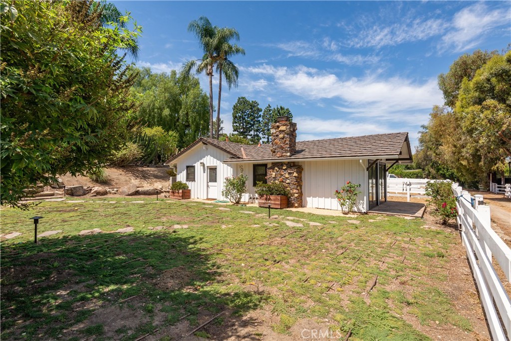 Single-story white house with a stone chimney, covered patio, and white-fenced yard.