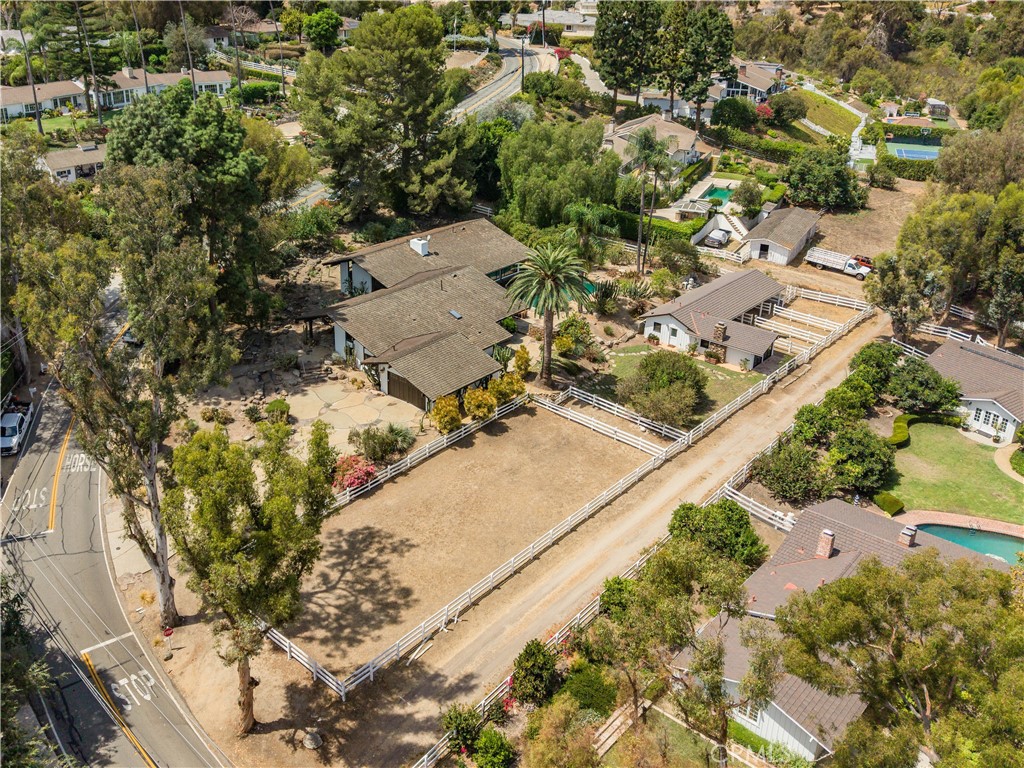 Aerial view of a ranch-style home, fenced paddock, outbuildings, and mature trees.