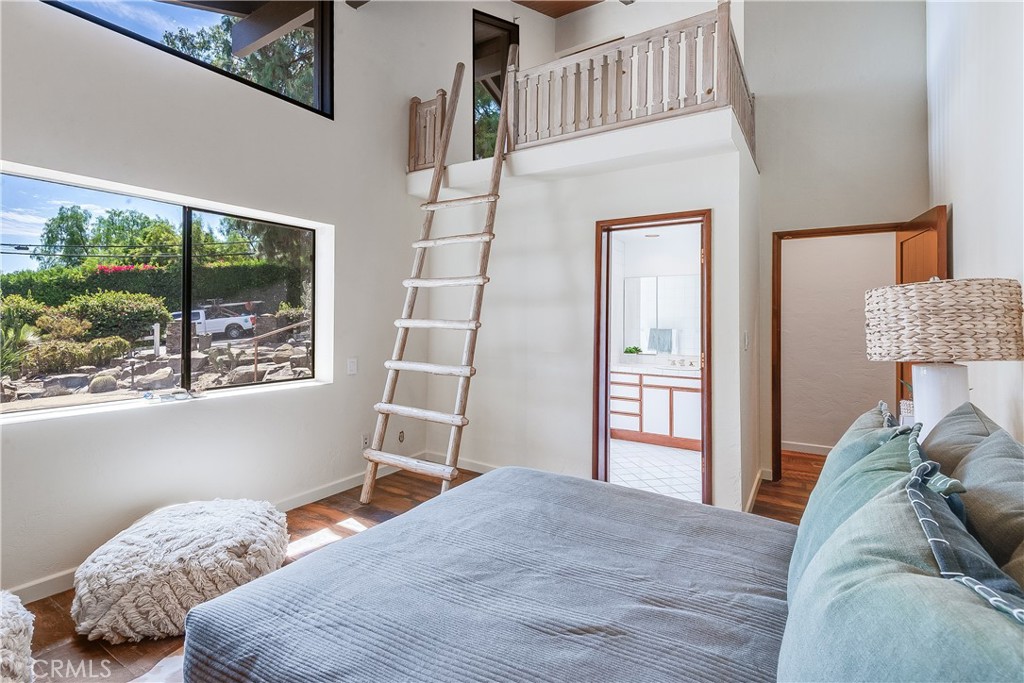 Bedroom with a wooden loft ladder, upper railing, and large windows overlooking greenery.