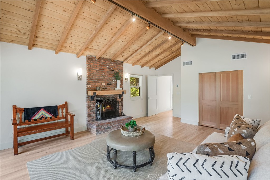 Living room with a brick fireplace, vaulted wood ceiling, and furnished seating area.