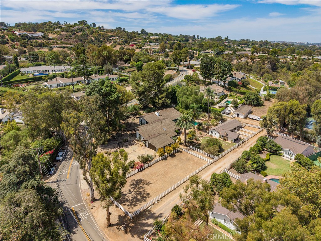 Aerial view of a fenced equestrian property with a riding arena among homes and rolling hills.