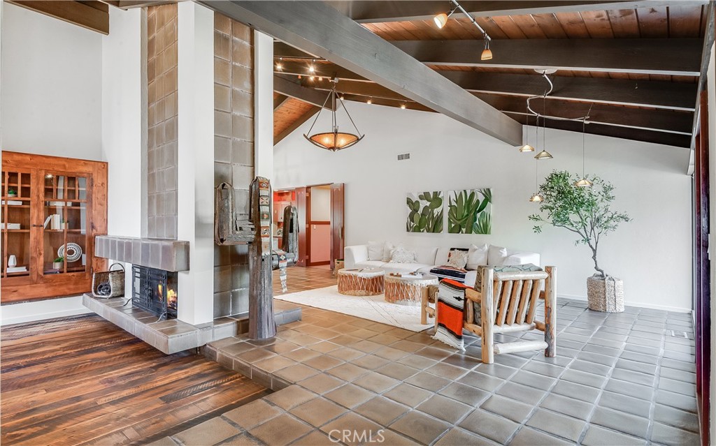 Living room with exposed beams, a tiled fireplace, built-in shelving, and a white sofa.