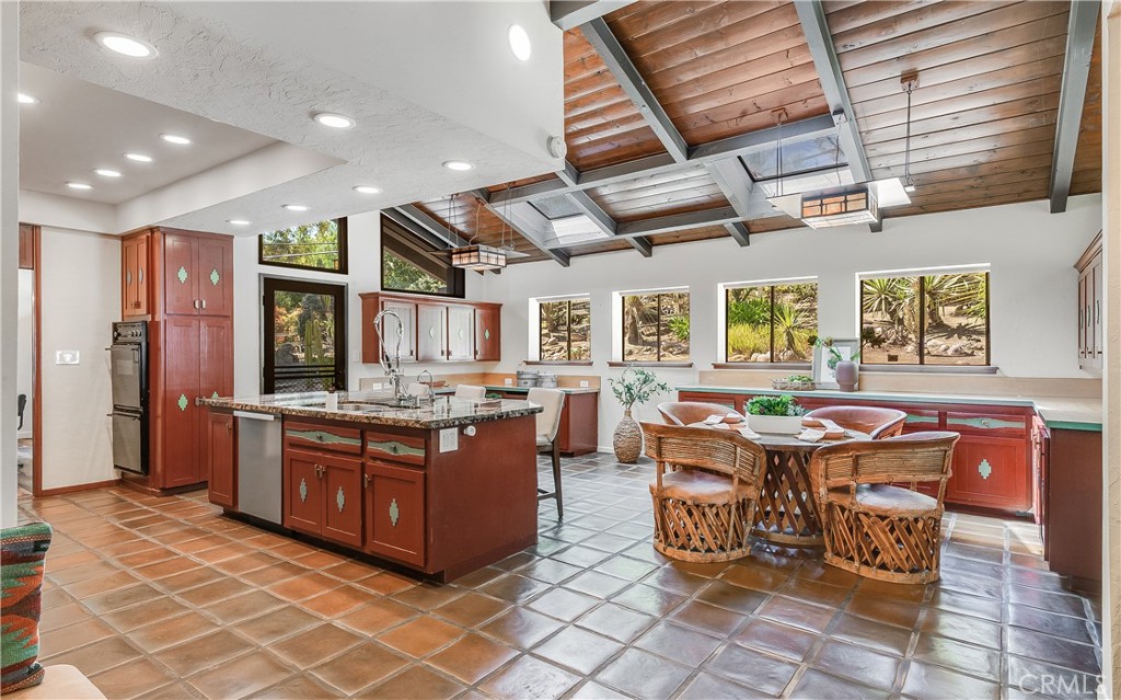 Kitchen with a central island, terracotta tile floors, exposed wood beams, and garden views.