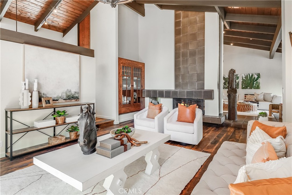 Living room with a tall tiled fireplace, vaulted wood ceiling, and white seating with orange accent pillows.