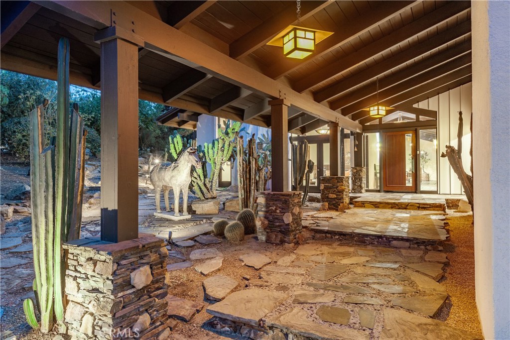 Covered home entry with exposed timber beams, lanterns, a flagstone path, and tall cacti.