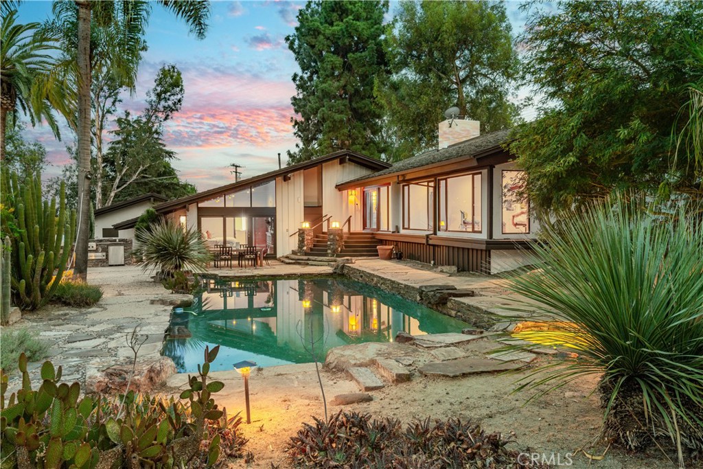 Rear view of a modern home with a swimming pool and stone patio at dusk.
