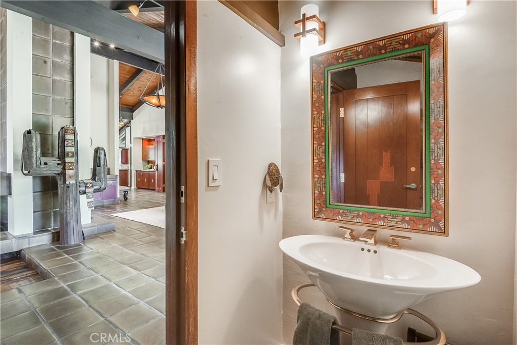 Bathroom basin beneath an ornate framed mirror, with a tiled doorway opening toward the kitchen.