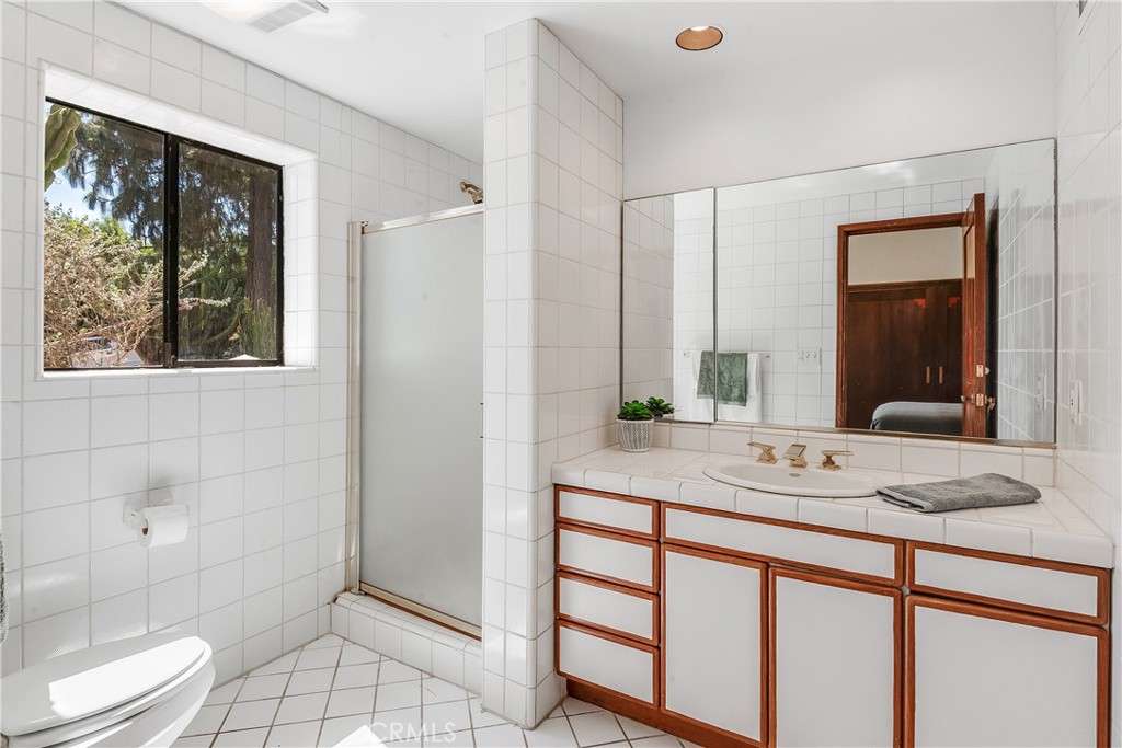 Tiled bathroom with a glass shower, mirrored vanity, and a window overlooking trees.