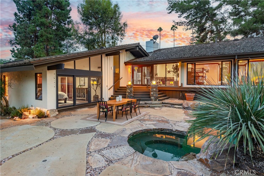 Home’s rear patio and small pool at dusk, with an outdoor dining set and warmly lit glass doors.