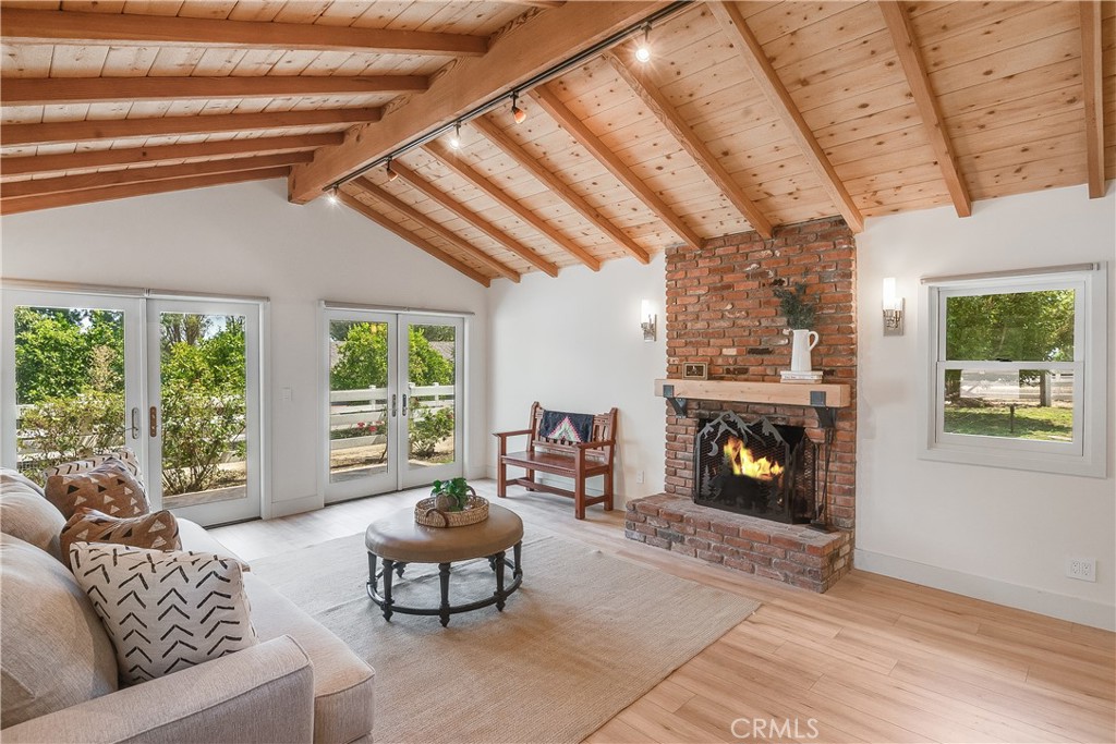 Living room with a vaulted wood ceiling, brick fireplace, and glass doors to a leafy yard.