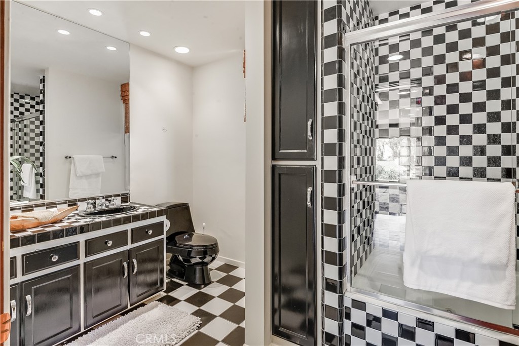 Bathroom with checkerboard tile, dark vanity cabinetry, and a glass-enclosed shower.