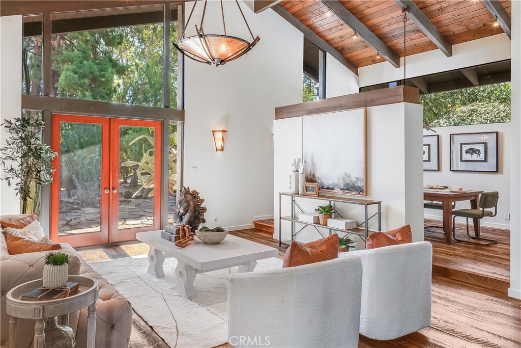 Living room with a vaulted wood ceiling, red-framed glass doors, and an adjacent dining area.