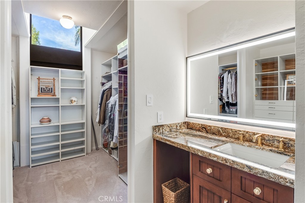 Walk-in closet and dressing area with built-in shelves, hanging clothes, and a granite-topped vanity.