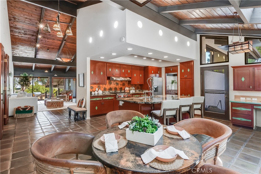 Open kitchen and dining area with reddish wood cabinetry, granite island, and vaulted wood ceiling.