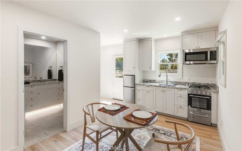 Bright white kitchen with stainless appliances and a set round dining table; vanity visible through the doorway.