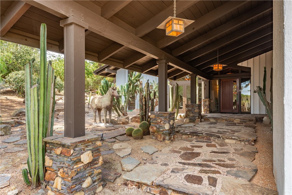 Covered stone entry with exposed timber beams, lanterns, cacti, and a horse statue.