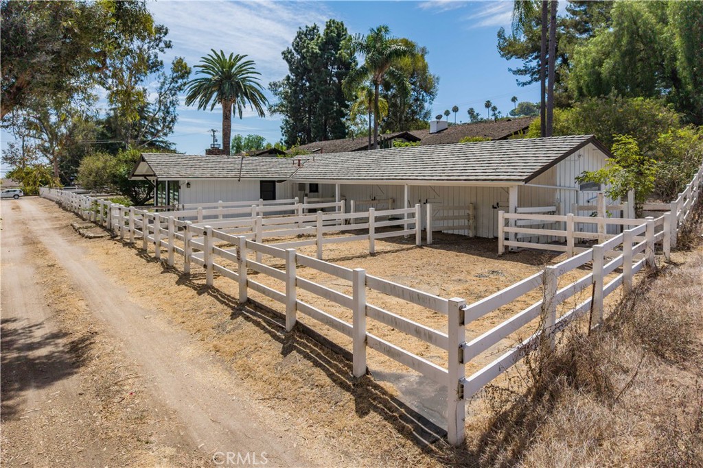 White equestrian stable and dry fenced paddocks beside a dirt lane, surrounded by mature trees.