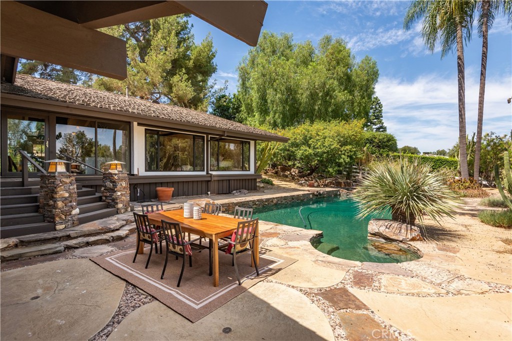 Backyard pool beside a stone patio with outdoor dining furniture and a single-story home.