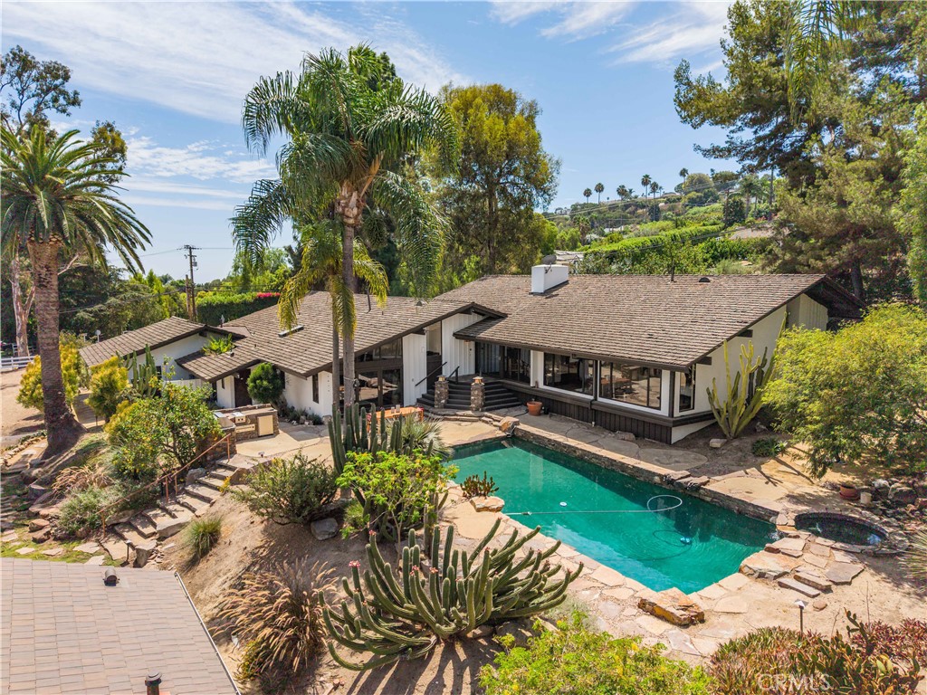 Single-story home with a turquoise pool and stone patio surrounded by palms and mature landscaping.