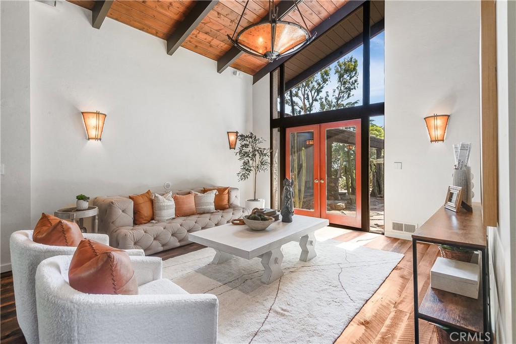 Living room with a vaulted wood ceiling, tufted sofa, and tall windows beside red-orange doors.