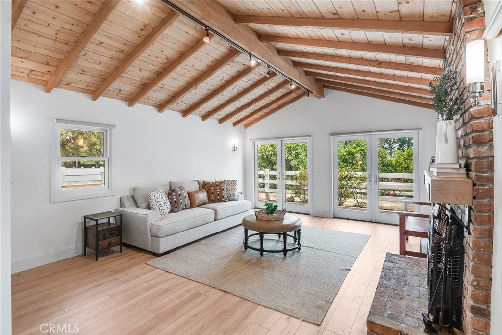Living room with exposed wood ceiling beams, brick fireplace, and glass doors to the garden.