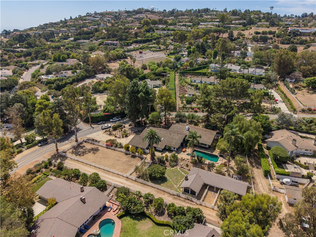 Aerial view of a home with a pool and fenced grounds amid rolling hills and neighboring homes.