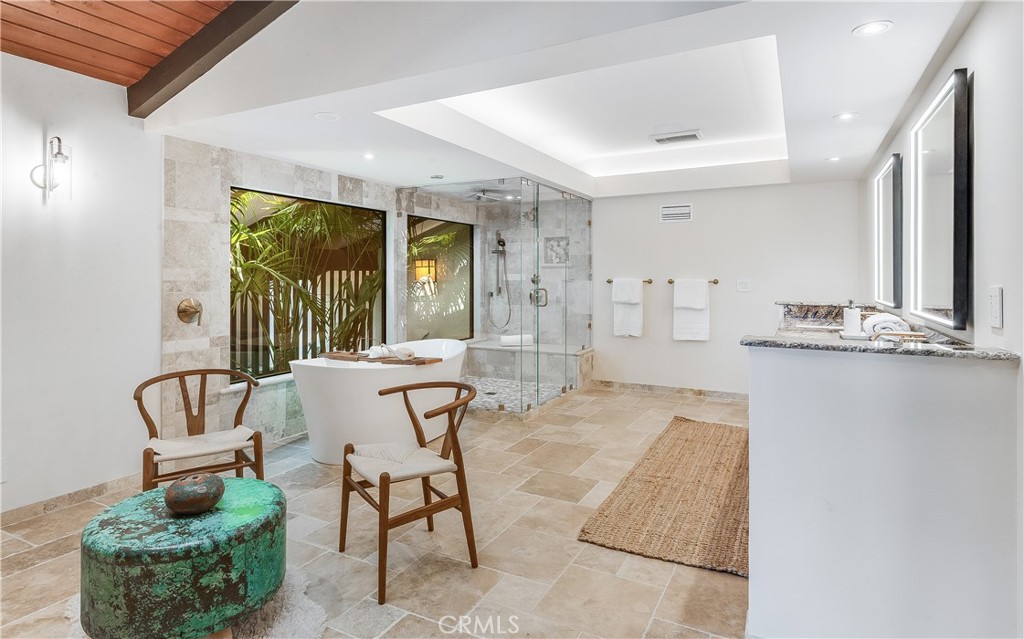 Primary bathroom with a freestanding tub, glass shower, large windows, and stone tile.