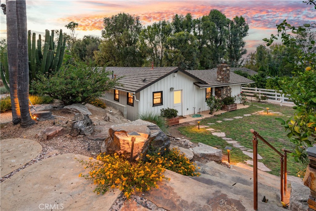 Single-story white house with a stone chimney and landscaped yard at sunset.