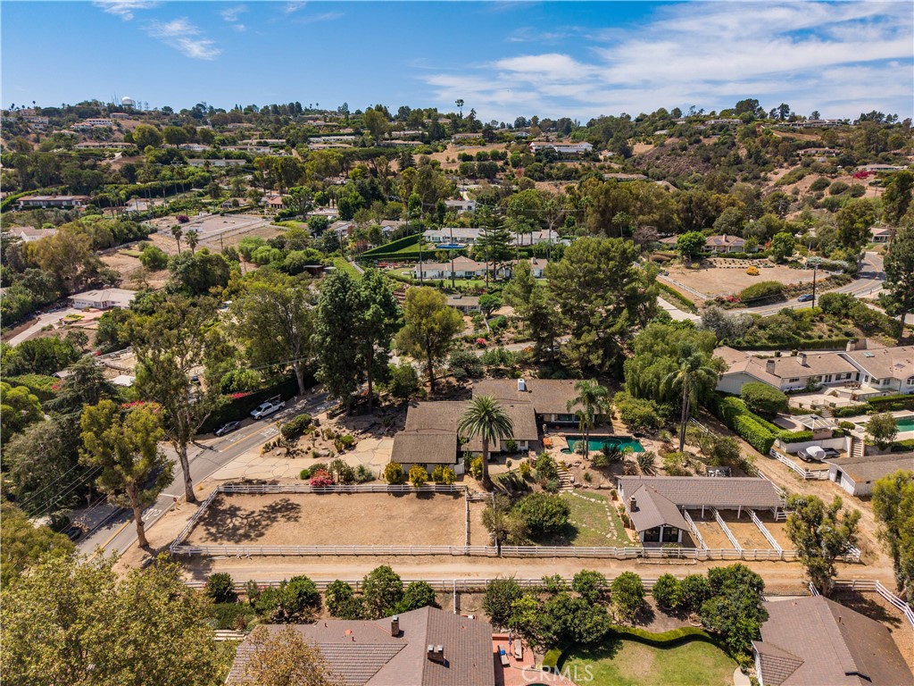 Aerial view of a home with a fenced riding arena, pool, and surrounding hillside neighborhood.