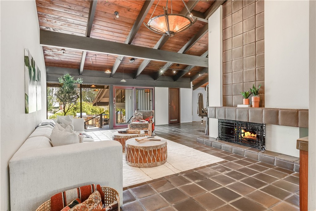 Living room with exposed wood ceiling, tiled fireplace, white sofa, and glass doors to a balcony.