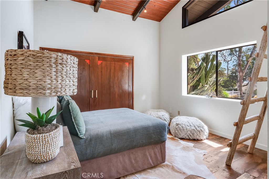 Bedroom with a low bed, exposed wood ceiling, and a large window overlooking cactus and trees.